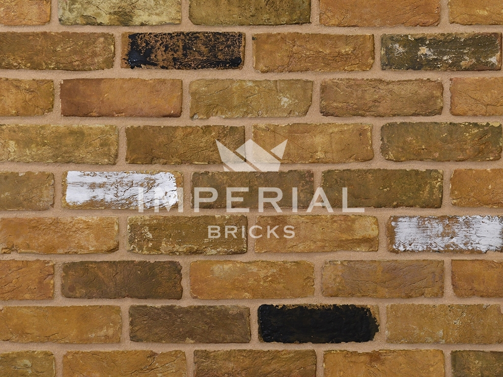 Reclamation Yellow Stock handmade bricks shown in a wall. The bricks are yellow with varying tones of weathering, and some black and white faces.