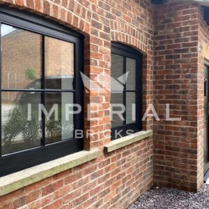 Angled view of the front of a residential new build home, built using Urban Weathered handmade bricks. A black door and windows are highlighted by decorative brick arches above.