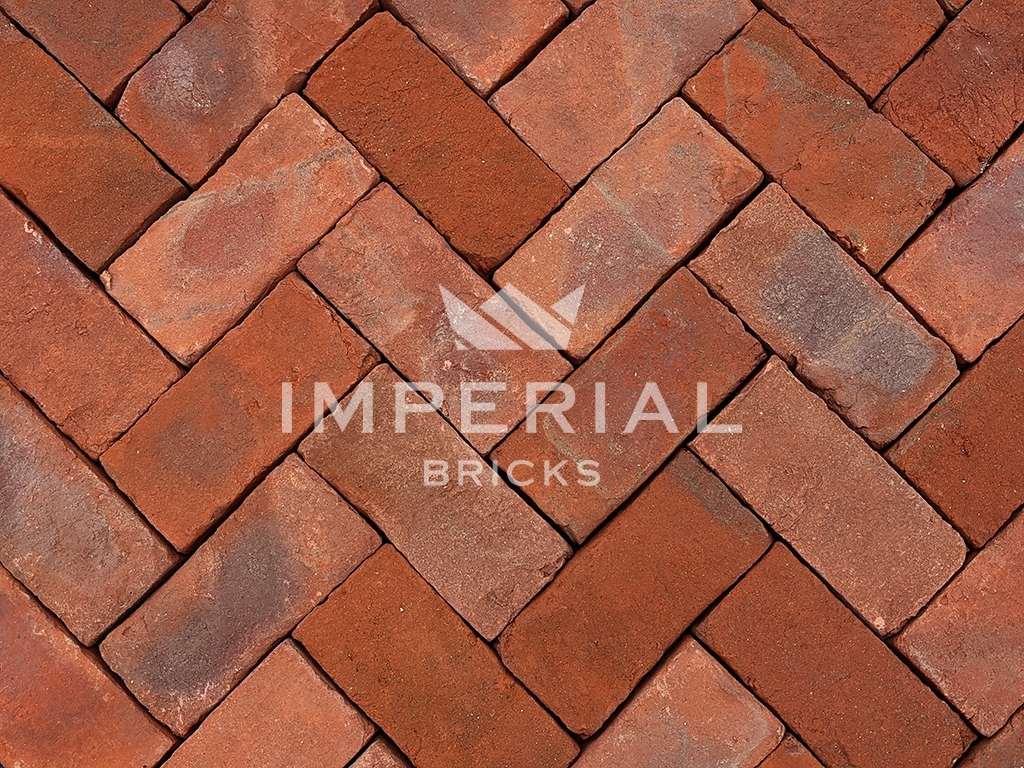 Hampton Blend handmade pavers laid in a herringbone pattern. The pavers are a blend of red and orange with subtle weathering on the faces and a sandy creased texture.
