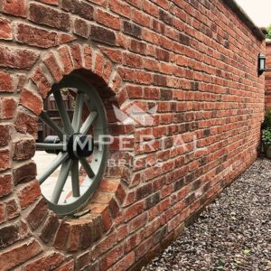 Close up, side angle view of a garden wall built using Country Blend handmade bricks, laid in stretcher bond. A decorative wheel is featured in the centre of the wall with bricks laid in a circle around it.