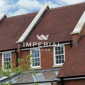 Red sandfaced machine made plain tiles shown on the roof of a terraced residential property.