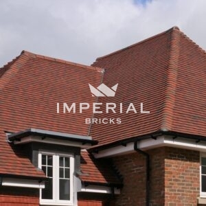 Weathered Red machine made plain roof tiles shown on the roof of a detached residential property.