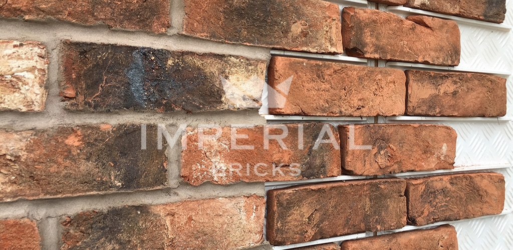 Handmade brick slips being applied to an external cladding system. the slips to the left are finished and mortared, the slips to the right side are not.