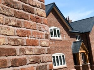 Close up angled view of a wall with a new build residential home in the background, built using Tumbled Regency Multi handmade bricks.