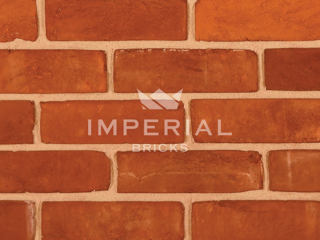 Regency Red Multi handmade bricks shown in a wall. The bricks are red blended with some oranges. Zoomed in to show the detail.