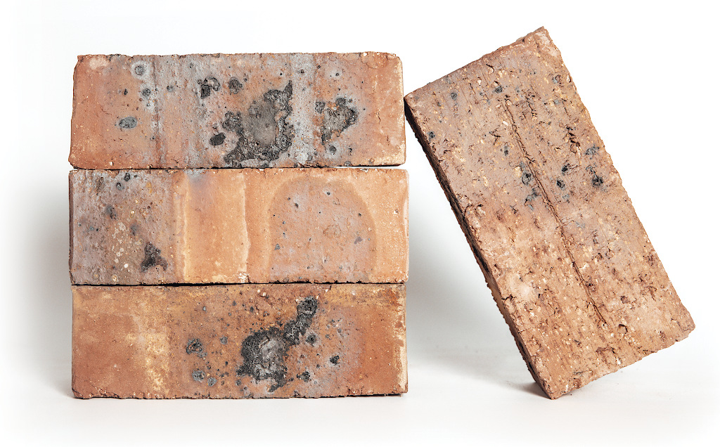 Three extruded wirecut bricks stacked horizontally. A fourth brick leans against the right side at an angle, showing its drag-faced texture on the top surface.