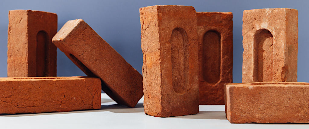 Standard metric size handmade bricks artfully laid out in front of a grey background.