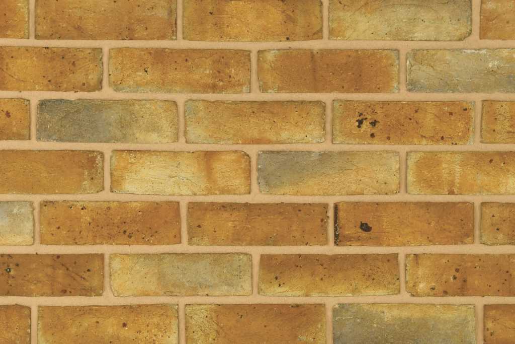 A wall of yellow handmade bricks with light and dark colour tones, laid using buff colour mortar. The light mortar colour is accentuating the brick colours.