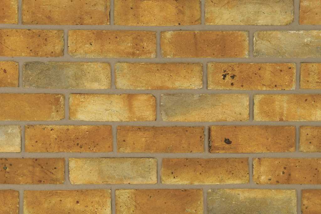 A wall of yellow handmade bricks with light and dark colour tones, laid using grey colour mortar. The dark mortar colour suppresses darker brick tones and accentuates the lighter ones.