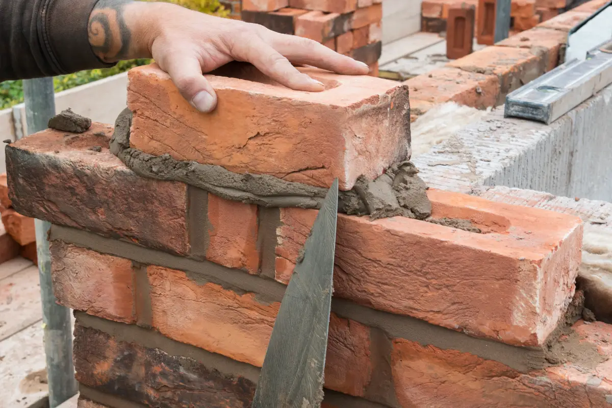 Weathered handmade frogged bricks being laid on a residential building site. The bricks are being laid with the brick frog facing up (uppermost), demonstrating how they should be laid in accordance with British Standard guidelines.