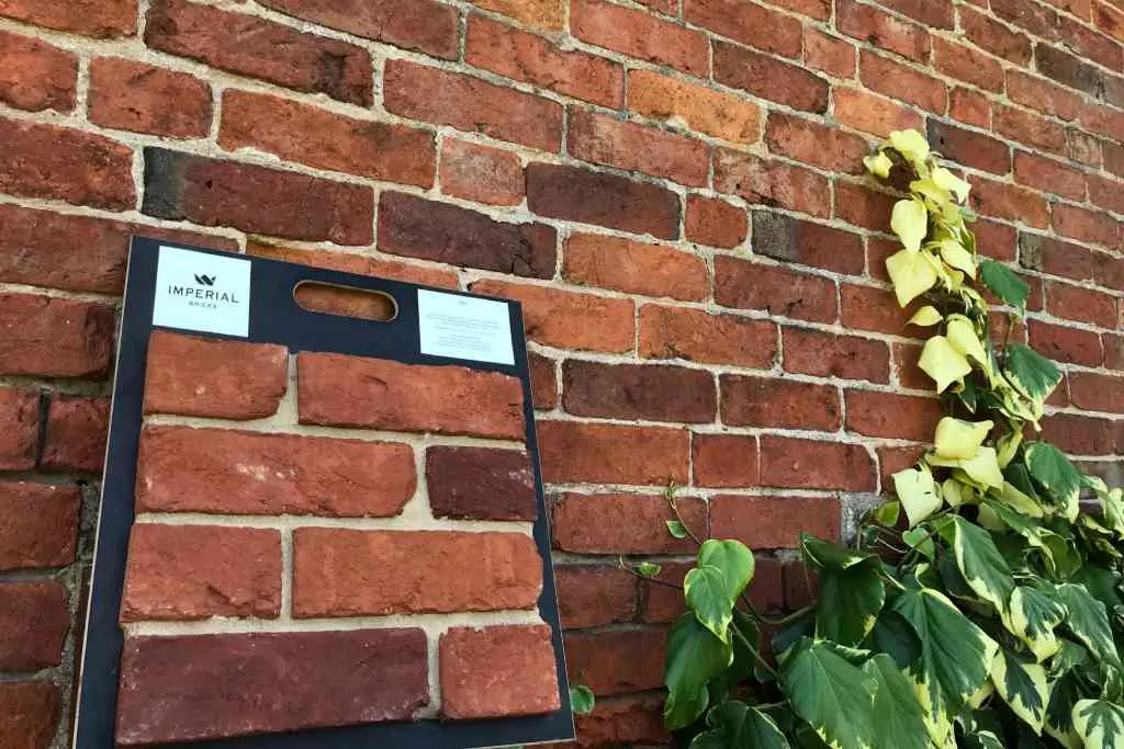 Example of a custom brick match by Imperial Bricks. A brick board with sample bricks is leaning against brickwork behind it. The sample bricks have been matched to the wall perfectly.