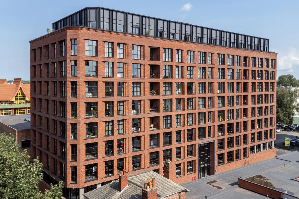 Street-level exterior view of One Silk Street in Manchester, showcasing handmade linear brickwork and large industrial-style windows.
